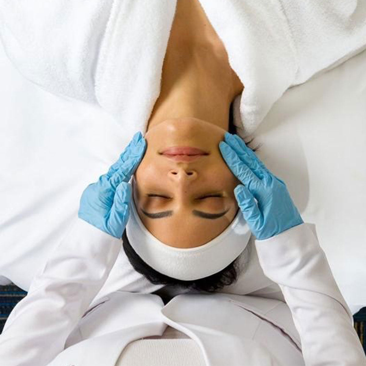 Person receiving a bespoke facial treatment with gloved hands gently massaging their temples.